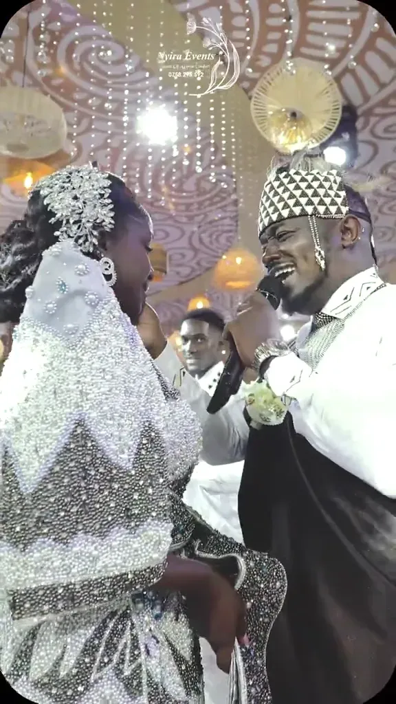A traditional ceremony under a patterned ceiling hung with woven pendants, the couple in kanzu and beaded gomesi entering through a sword arch.
