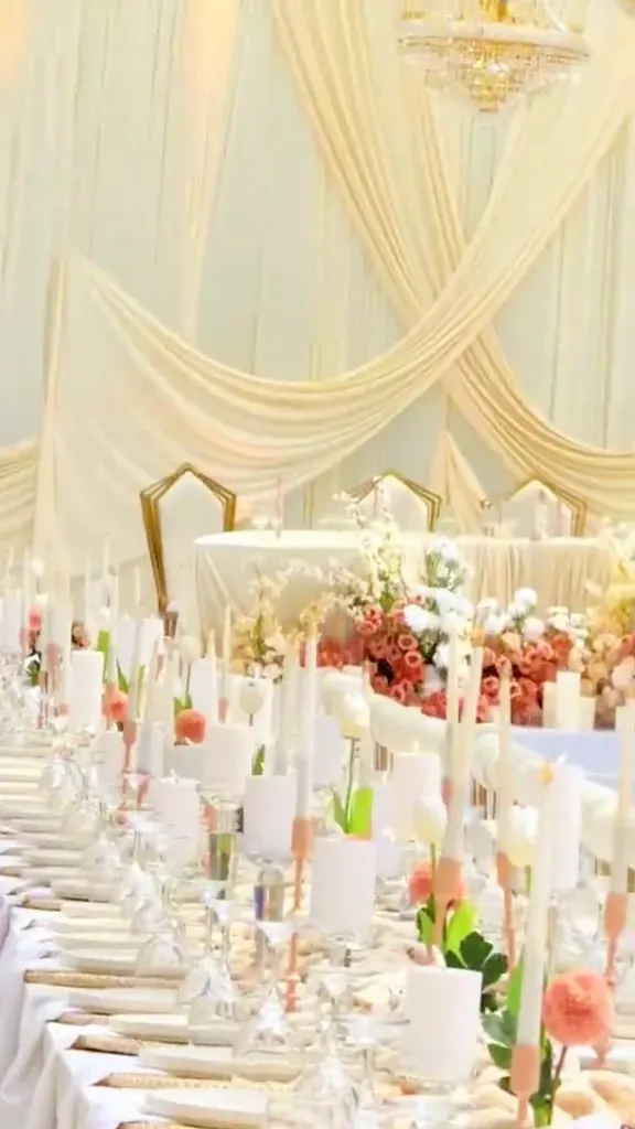 Long banquet tables in cream and gold under chandeliers and draped ceiling swags.