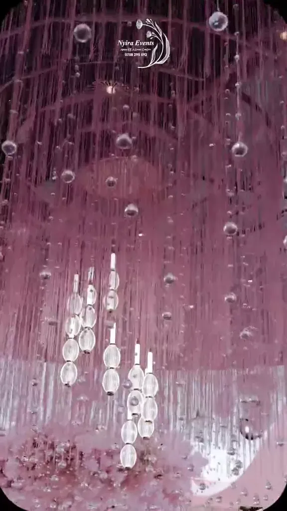 A ceremony dressed in blush and pink: draped walls, blossom installations, long tables with black bentwood chairs, the bride and her attendants in gomesi.