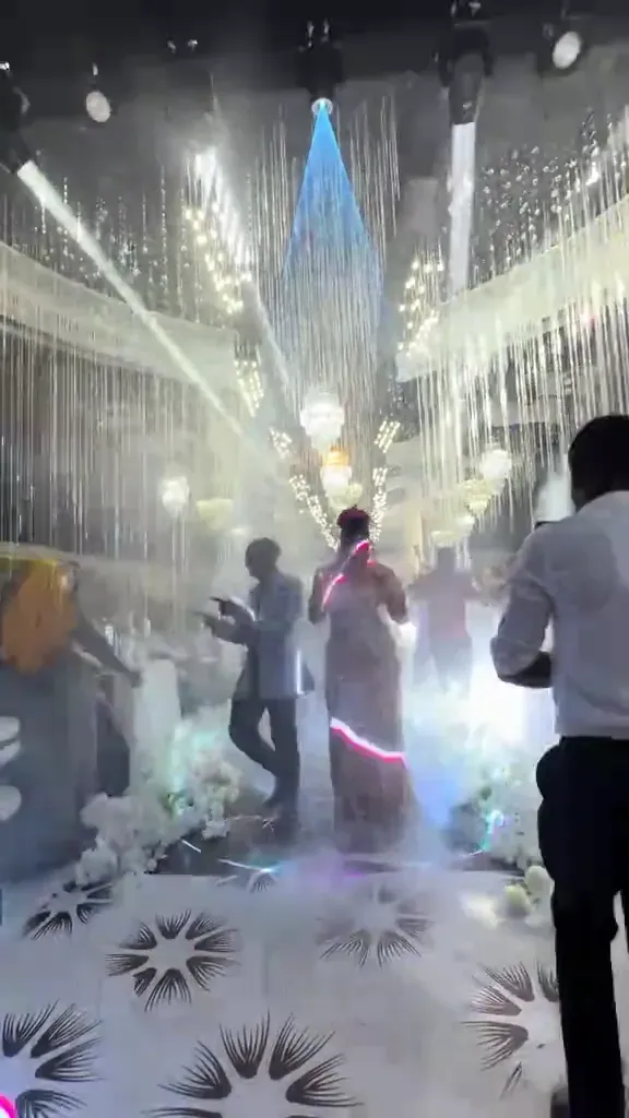 A reception at night under crystal strands and moving lights, haze across the dance floor.