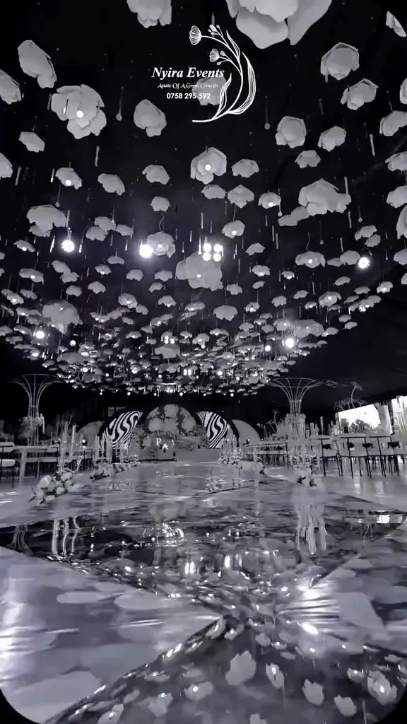 A wedding reception seen down the aisle toward a lit floral backdrop.