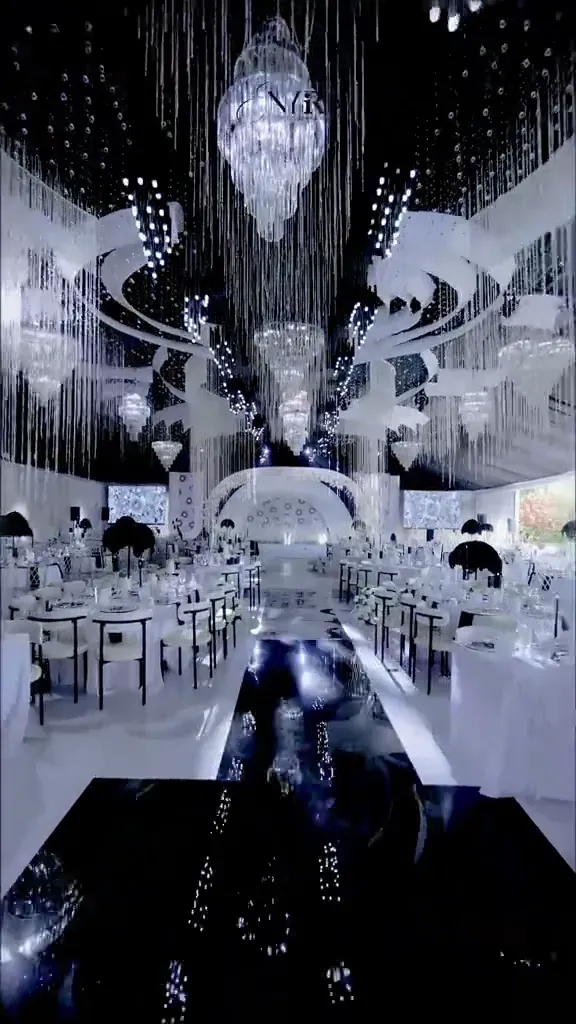 A wedding reception dressed entirely in white and black, long tables and a draped backdrop.