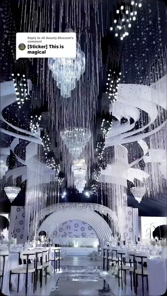 A hall hung with crystal strands over a fan-shaped white backdrop, black-framed chairs at round tables.